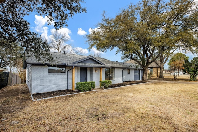 ranch-style home featuring a front lawn, roof with shingles, and brick siding