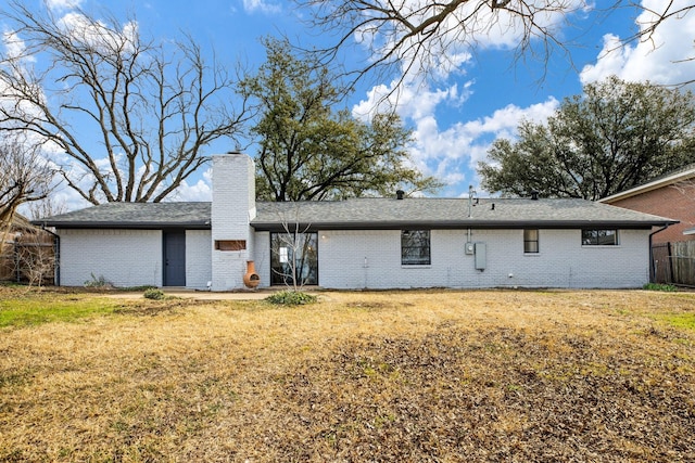 back of property featuring brick siding, fence, a chimney, and a lawn