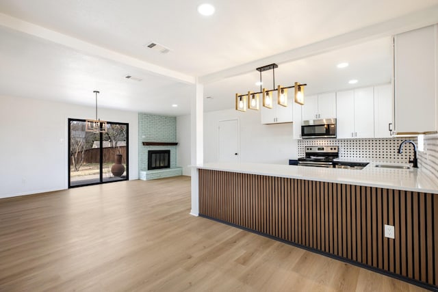 kitchen with light wood-style flooring, stainless steel appliances, a peninsula, a sink, and visible vents