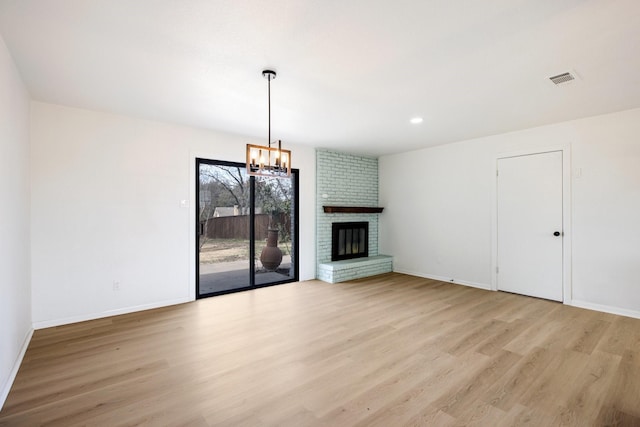 unfurnished living room featuring visible vents, baseboards, light wood-style flooring, a brick fireplace, and a notable chandelier