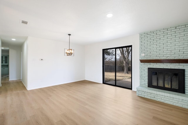 unfurnished living room featuring light wood-style floors, a fireplace, visible vents, and a chandelier