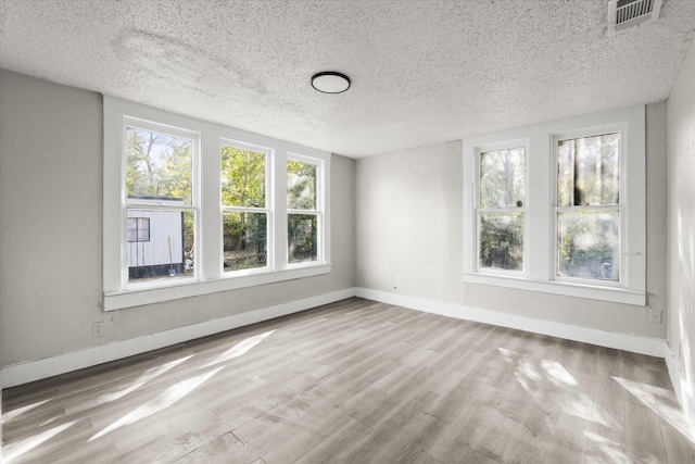 unfurnished room with a textured ceiling, wood finished floors, visible vents, and baseboards