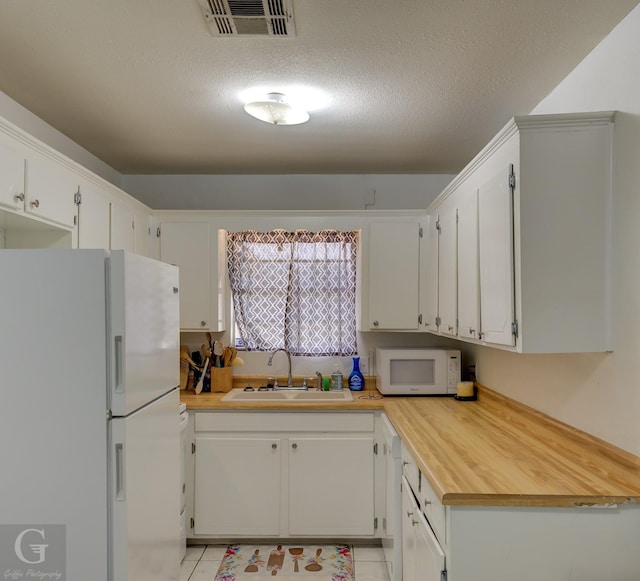 kitchen featuring light tile patterned floors, white appliances, a sink, and visible vents