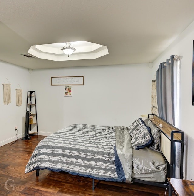 bedroom with a skylight, baseboards, visible vents, a raised ceiling, and wood finished floors