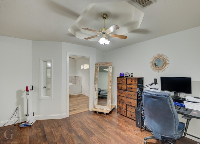 office with a tray ceiling, visible vents, a ceiling fan, wood finished floors, and baseboards