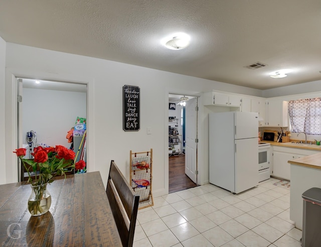 kitchen with white appliances, light tile patterned floors, visible vents, white cabinetry, and a sink