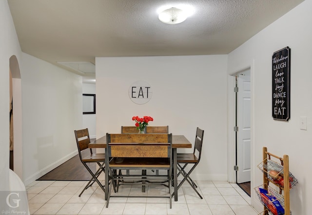 dining space featuring light tile patterned floors, baseboards, arched walkways, and a textured ceiling