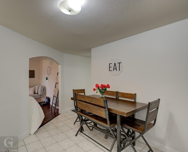 dining room featuring arched walkways, a textured ceiling, and light tile patterned floors