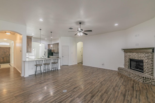 unfurnished living room with arched walkways, a fireplace, visible vents, dark wood-type flooring, and ceiling fan