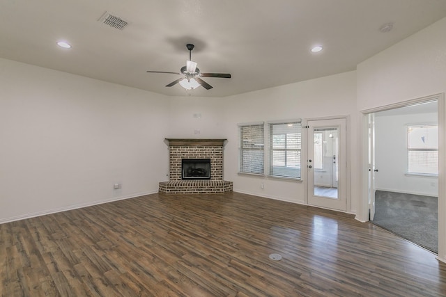 unfurnished living room featuring dark wood-type flooring, a brick fireplace, visible vents, and plenty of natural light