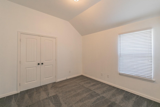 unfurnished bedroom with dark carpet, a closet, vaulted ceiling, and baseboards