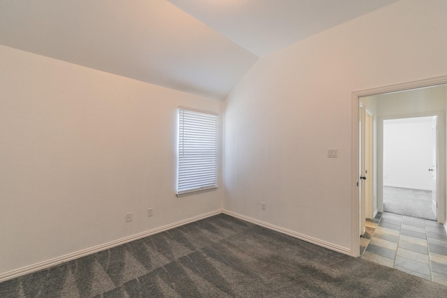 spare room featuring vaulted ceiling, dark colored carpet, and baseboards