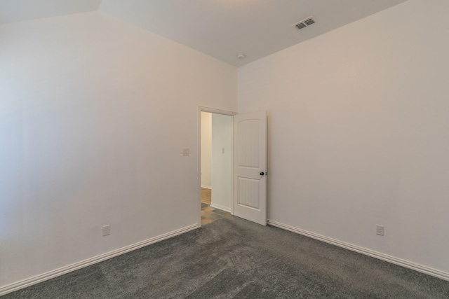 empty room featuring lofted ceiling, visible vents, dark carpet, and baseboards