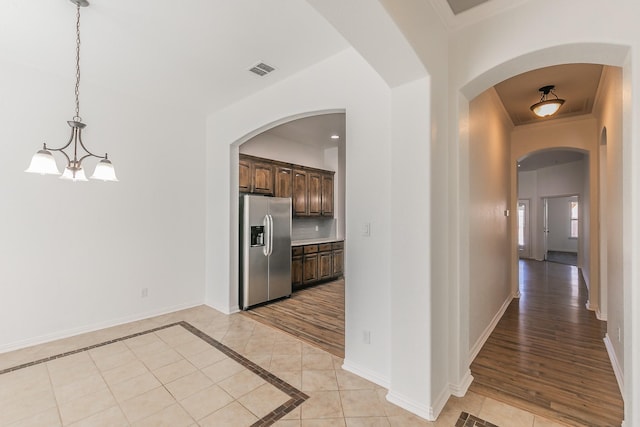 hallway featuring light tile patterned floors, a chandelier, visible vents, baseboards, and crown molding