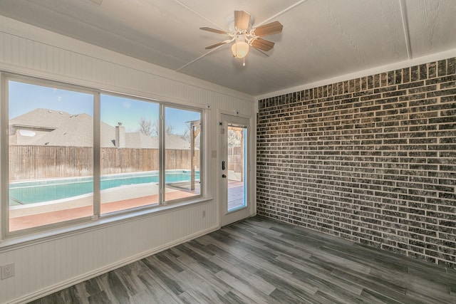 spare room with ceiling fan, brick wall, and wood finished floors