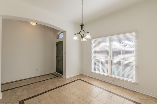 empty room with light tile patterned floors, an inviting chandelier, arched walkways, and baseboards