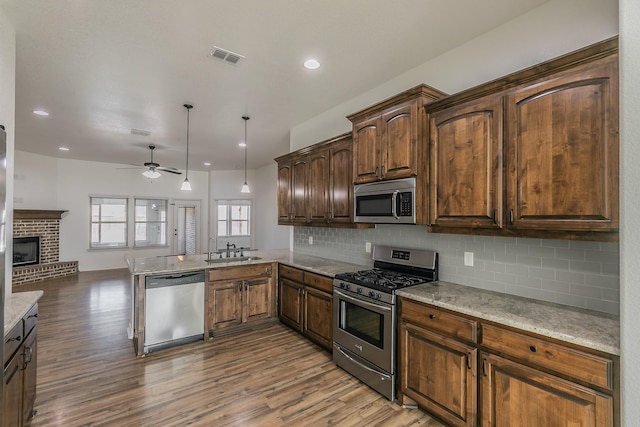 kitchen with a fireplace, stainless steel appliances, tasteful backsplash, a sink, and light wood-type flooring