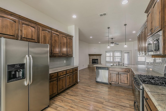 kitchen with open floor plan, stainless steel appliances, light wood-type flooring, a fireplace, and a sink