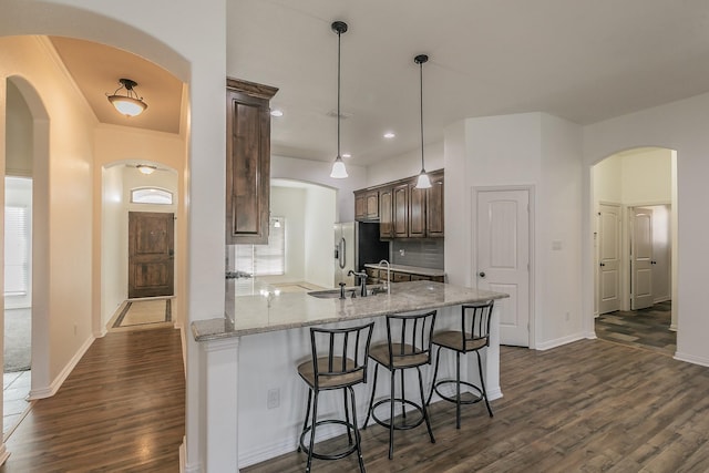 kitchen featuring a breakfast bar, dark wood finished floors, a sink, light stone countertops, and a peninsula