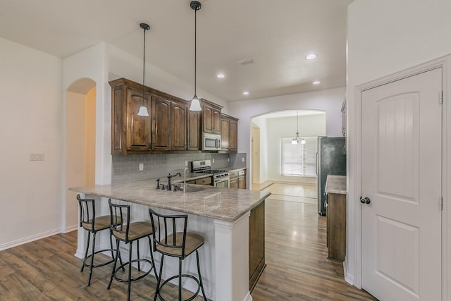 kitchen featuring arched walkways, backsplash, appliances with stainless steel finishes, a sink, and a peninsula