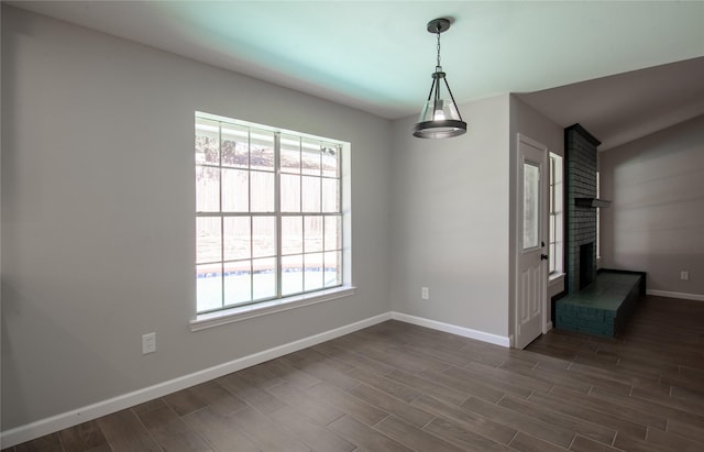 unfurnished dining area with a fireplace, baseboards, and dark wood-style flooring