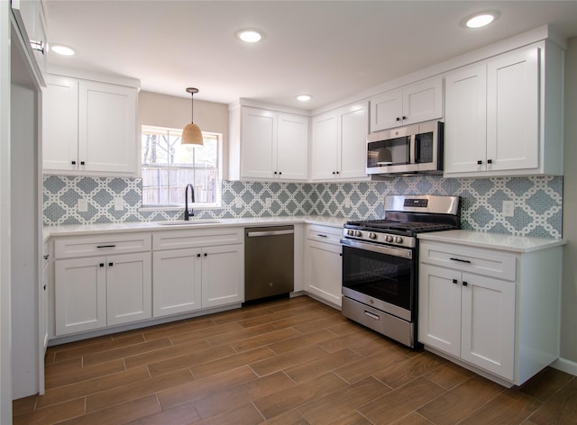 kitchen featuring white cabinets, appliances with stainless steel finishes, wood tiled floor, light countertops, and a sink