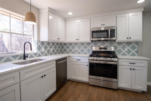 kitchen with appliances with stainless steel finishes, wood tiled floor, light countertops, white cabinetry, and a sink