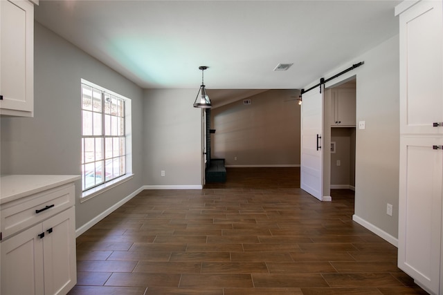 unfurnished dining area with visible vents, dark wood finished floors, baseboards, and a barn door