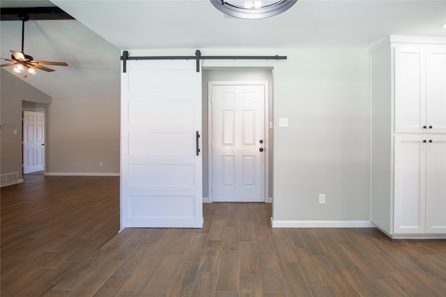 empty room featuring lofted ceiling, dark wood-style flooring, ceiling fan, and a barn door