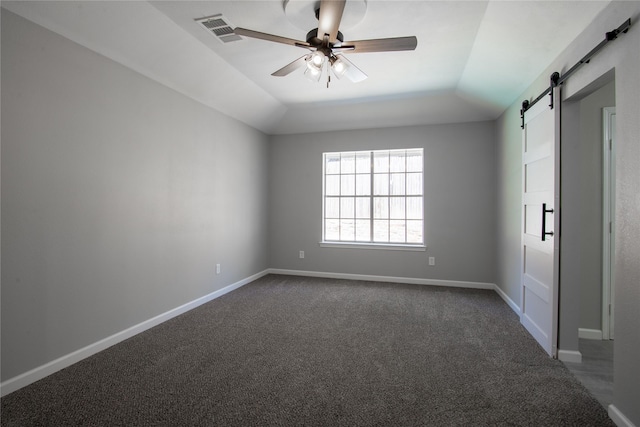 empty room with visible vents, dark carpet, a barn door, ceiling fan, and baseboards