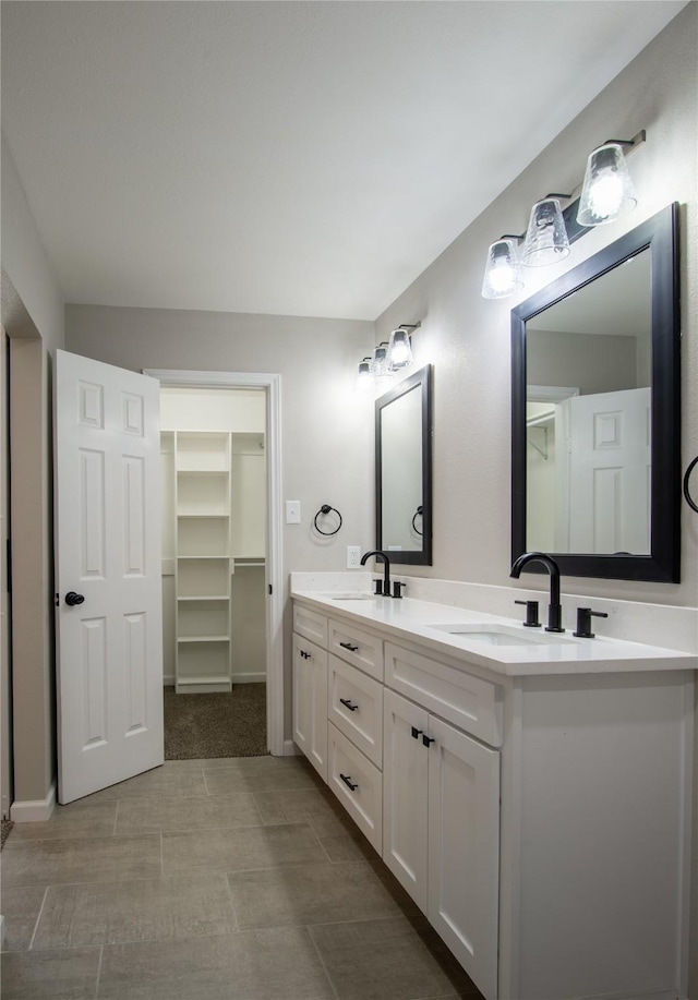 full bath with double vanity, baseboards, a walk in closet, and a sink