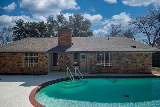 rear view of house featuring brick siding, a patio, a chimney, roof with shingles, and an outdoor pool