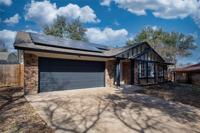 view of front of property with a garage, solar panels, concrete driveway, fence, and brick siding