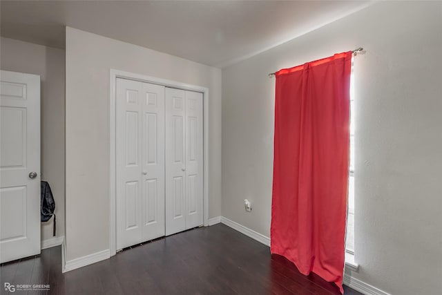 unfurnished bedroom with dark wood-style floors, a closet, and baseboards