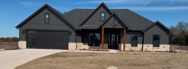 view of front of house featuring a garage, driveway, stone siding, roof with shingles, and board and batten siding