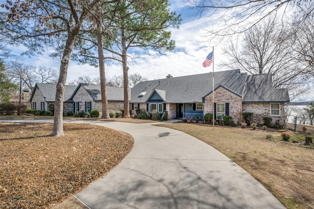 view of front of home with a shingled roof, concrete driveway, a chimney, a front lawn, and brick siding