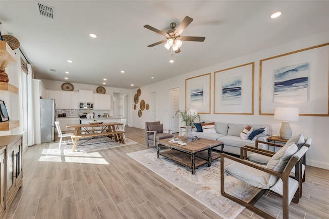 living room with visible vents, baseboards, ceiling fan, light wood-style floors, and recessed lighting