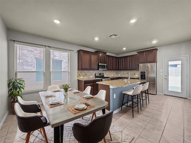 kitchen with light tile patterned floors, stainless steel appliances, visible vents, decorative backsplash, and a kitchen island with sink