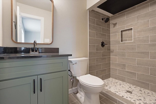 bathroom with a tile shower, vanity, and toilet