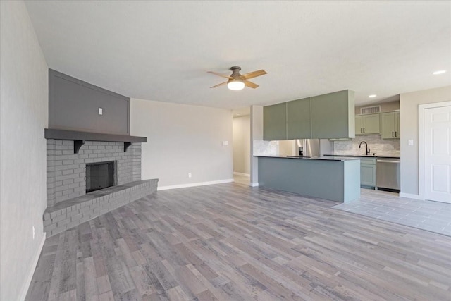 unfurnished living room featuring a brick fireplace, a sink, light wood finished floors, and ceiling fan