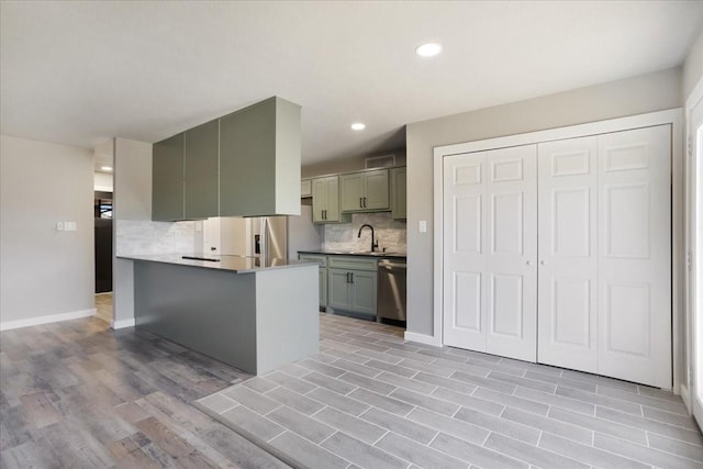 kitchen featuring light wood-style flooring, stainless steel appliances, a peninsula, a sink, and backsplash