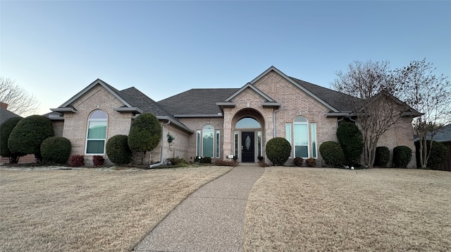 view of front of home with a shingled roof, brick siding, and a front lawn