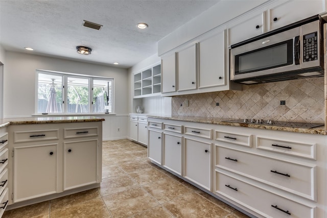 kitchen featuring a textured ceiling, black electric cooktop, visible vents, decorative backsplash, and stainless steel microwave