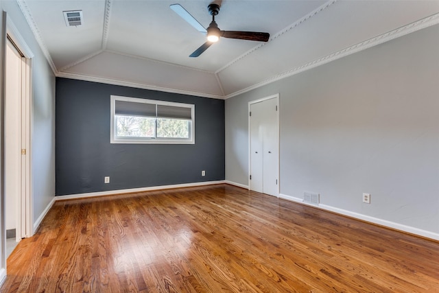 spare room with visible vents, vaulted ceiling, crown molding, and wood finished floors