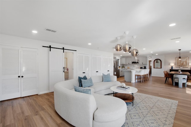 living area featuring a barn door, visible vents, light wood-style flooring, and recessed lighting