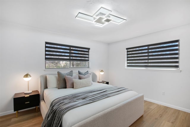 bedroom with multiple windows, baseboards, and wood finished floors