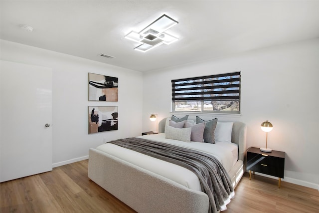 bedroom with wood finished floors, visible vents, and baseboards