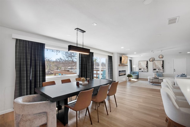 dining space featuring light wood-type flooring, visible vents, a fireplace, and baseboards