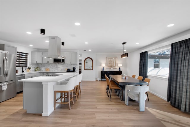 kitchen featuring tasteful backsplash, island range hood, stainless steel appliances, light countertops, and a kitchen bar