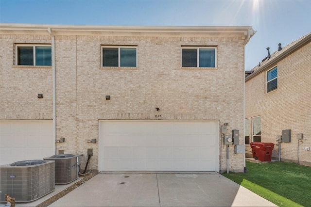 back of house with a garage, central AC, brick siding, and driveway